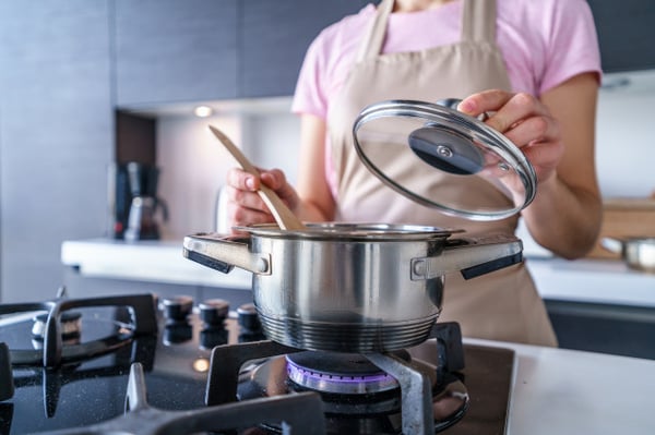 woman-housewife-apron-using-steel-metal-saucepan-preparing-dinner-kitchen-home_122732-2425