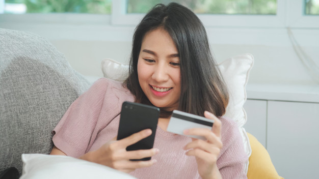 young-smiling-asian-woman-using-smartphone-buying-online-shopping-by-credit-card-while-lying-sofa-when-relax-living-room-home-lifestyle-latin-hispanic-ethnicity-women-house-concept_7861-1952