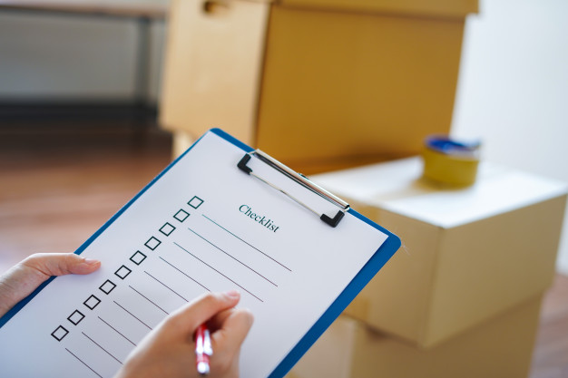 close-up-hand-with-checklist-cardboard-box-before-moving-new-location_123441-69