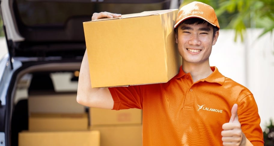 lalamove driver wearing orange shirt and a cap showing thumbs up while carrying a box-1