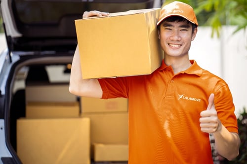 lalamove driver wearing orange shirt and a cap showing thumbs up while carrying a box
