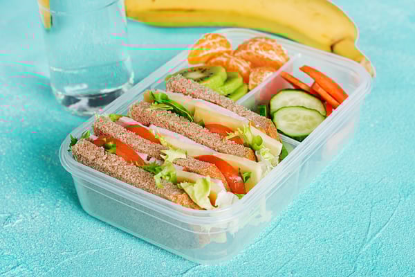 school-lunch-box-with-sandwich-vegetables-water-fruits-table