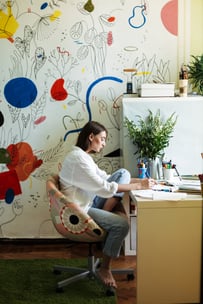 young-painter-white-shirt-sitting-desk-thoughtfully-drawing-picture-with-big-colorful-patterns-canvas-background-home