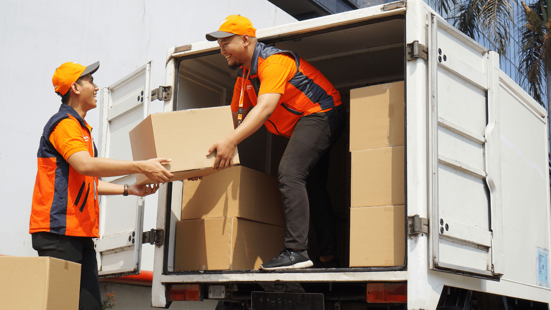two lalamove delivery partners wearing orange shirt and orange cap carries a box into a white lorry (1)